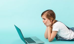 Flicka som ligger framför en bärbar dator