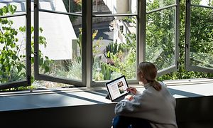 Kvinna som sitter vid ett skrivbord bredvid ett fönster och arbetar på hennes bärbara dator