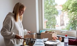 MDA-Frysare-Ung kvinna packar ut köksredskap ur lådor på ett bord vid ett fönster