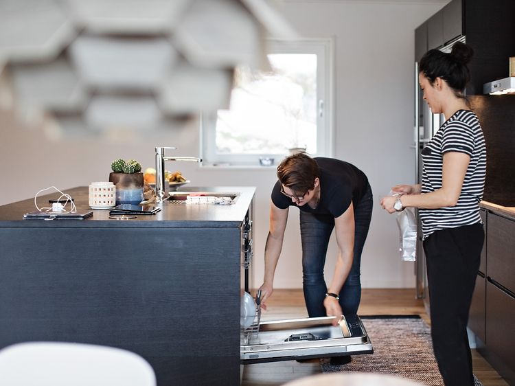 Ett par i ett modernt kök ställer in disk i en integrerad diskmaskin