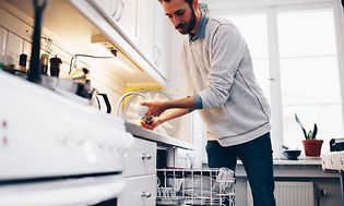 Man sköljer en kopp och står framför en öppen diskmaskin