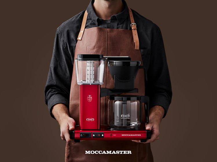 Man i förkläde håller en Moccamaster kaffebryggare