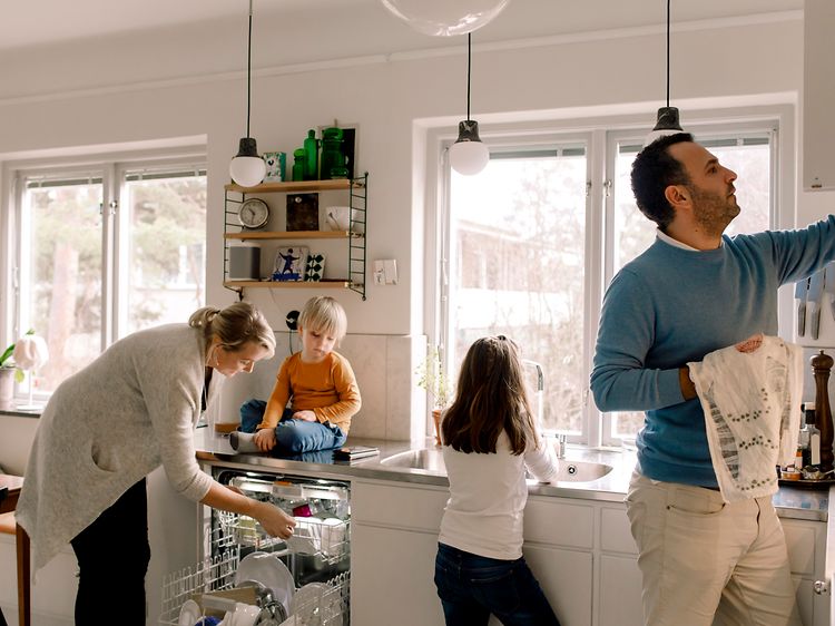 Familj i ett kök som tar ut ren disk ur diskmaskinen.