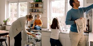 Familj i ett kök som tar ut ren disk ur diskmaskinen.