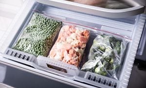 Tre plastpåsar med infrysta grönsaker i en frys