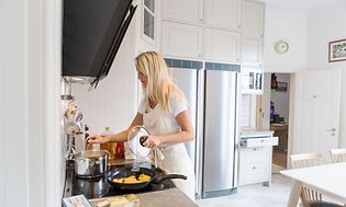 Kvinna lagar mat i ett kök med ett kylskåp och en frys i bakgrunden