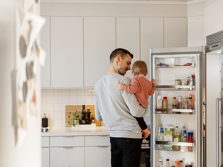 En pappa med sin dotter i ett kök bredvid en öppen kyl