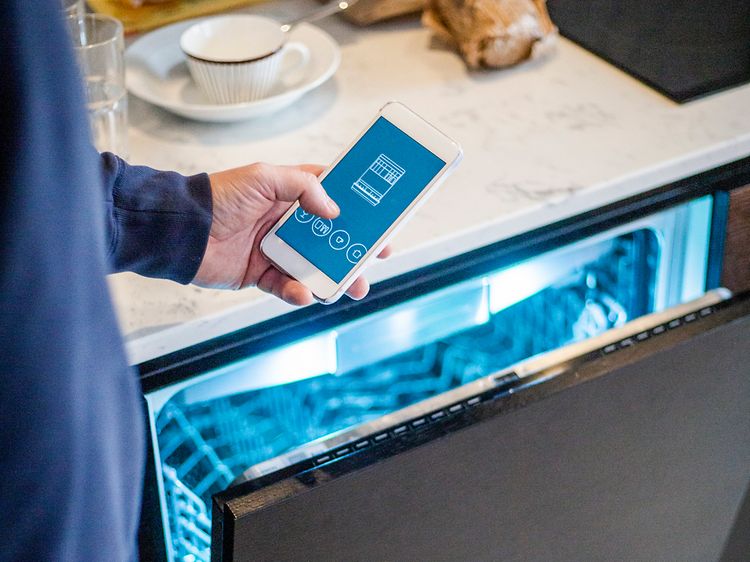 Man håller sin smartphone framför en halvöppen diskmaskin med belysning