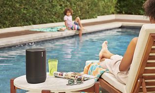 Sonos Move på ett bord vid en pool bredvid en kvinna i en solstol