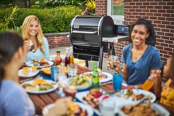 Personer som äter middag och en Weber pelletsgrill i bakgrunden