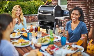 Personer som äter middag och en Weber pelletsgrill i bakgrunden