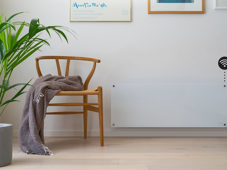 Smart panel heater on a wall with a wooden chair and plant in front