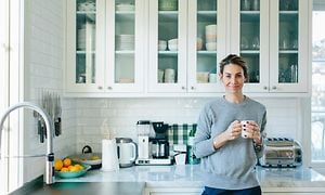 En kvinna står i ett kök med en kaffekopp i handen