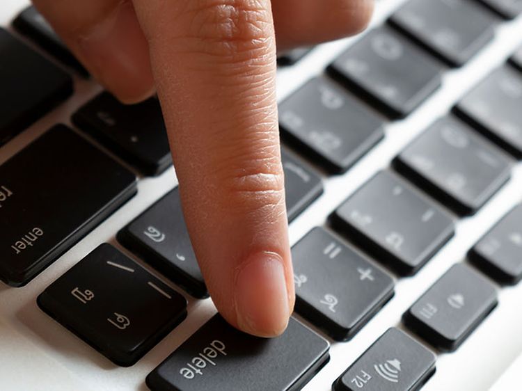En hand som trycker på delete-knappen på en bärbar dator