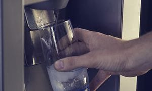 En person som fyller upp ett glas med vatten från en integrerad vattendispenser i en kyl
