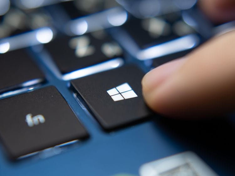 Ett finger trycker på Microsoft Windows-logotypen på en blå bärbar dator.