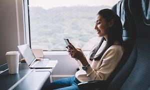 Kvinna använder mobil på ett tåg med en laptop framför henne
