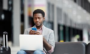 Man använder mobilen med en dator i famnen