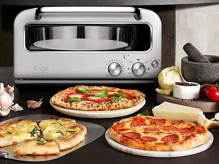 Olika typer av pizza på ett bord och en Sage pizzaugn i bakgrunden