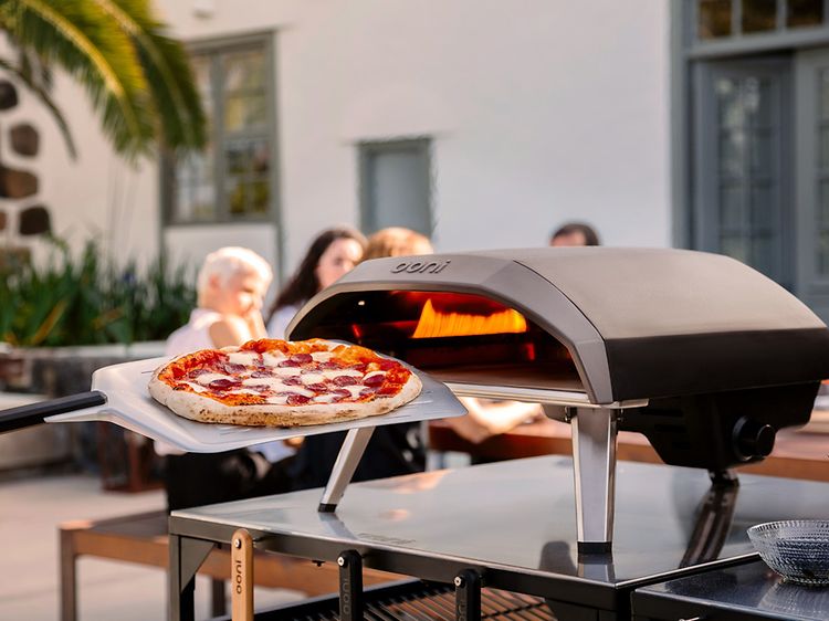 En pizza framför en pizzaugn och människor i bakgrunden.