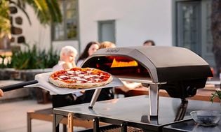 En pizza framför en pizzaugn och människor i bakgrunden.