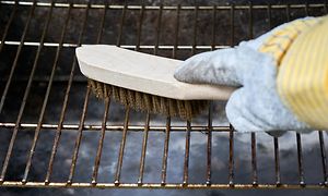 Hand som håller en rengöringsborste och rengör grillen