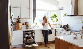 Kvinna står och pratar i telefonen i ett kök med en öppen integrerad diskmaskin