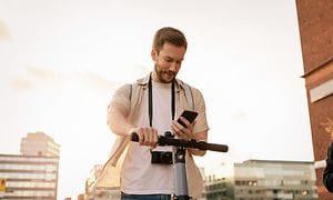 Wearables - Manlig turist som står still med elsparkcykel och kollar på sin mobiltelefon