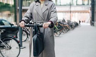 Wearables - Affärskvinna som åker på en elsparkcykel med datorväska på styret