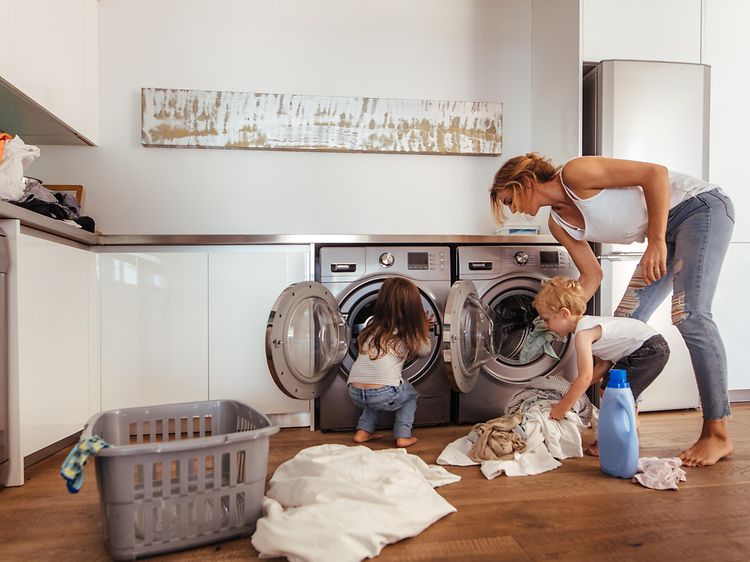 Kvinna och två barn lägger in tvätt i tvättmaskiner i en tvättstuga