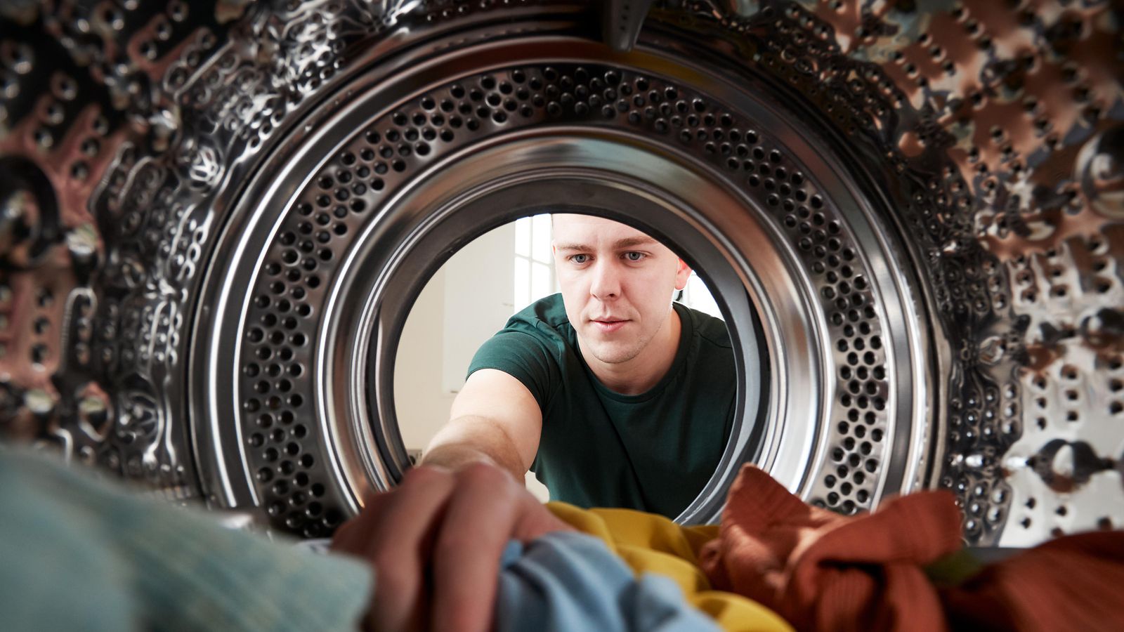Man lägger in kläder i en tvättmaskin, sett inifrån tvättmaskinen