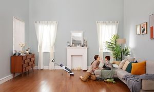 Roborock Dyad skaftdammsugare i ett rum, och en mamma som leker med sitt barn i soffan