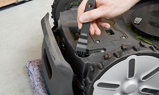 Hand som rengör under en robotgräsklippare
