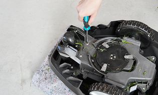 Robotgräsklippare och en hand med skruvmejsel