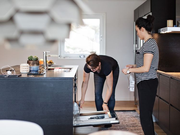 Två kvinnor står i ett kök hemma bredvid en öppen diskmaskin