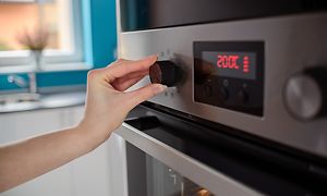 MDA-Ovens-Närbild på kvinnohand som justerar temperatur på en ugn