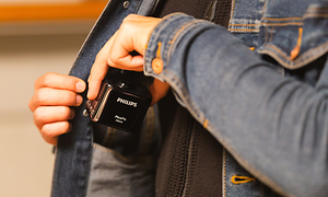 Man stoppar en portabel Philips projektor i innerfickan på en jeansjacka. Den är liten och svart med vit logga på.