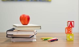 Böcker, pennor, abc-klossar och ett äpple staplat på ett bord.
