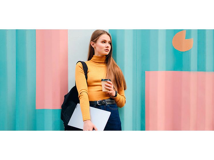 Flicka framför en målad vägg med Lenovo IdeaPad 5 och kaffe i händerna