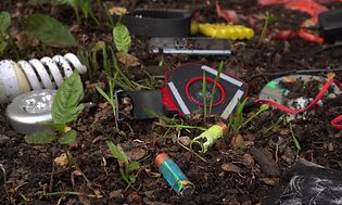 batterier, lampor och annat elavfall som ligger och skräpar i jord med blad som sticker upp.
