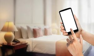 Händer som håller i en smartphone i ett sovrum