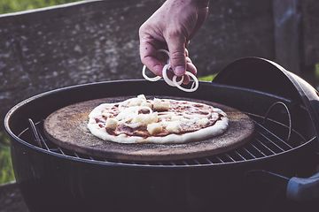 En hand som lägger topping på en pizza