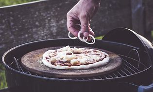 En hand som lägger topping på en pizza