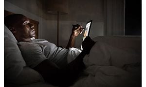 Man som ligger i sängen och arbetar med en digital penna på en skärm