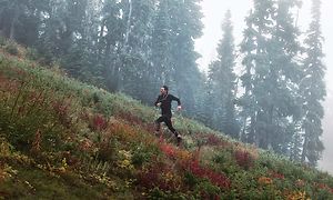 Man som springer upp en backe i skogen