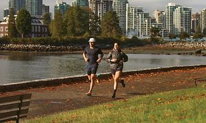 Två joggare som springer i en park bredvid ett vatten