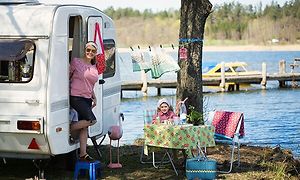 Kvinna stiger ut ur en husvagn bredvid en liten flicka som sitter vid ett campingbord