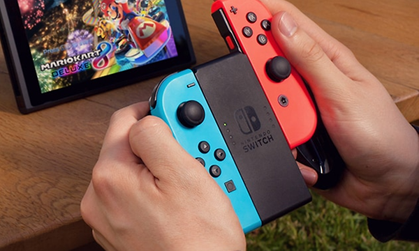 Handhållen Nintendo Switch-enhet med två joycons. På bildskärmen i bakgrunden syns Mariokart Deluxe. 