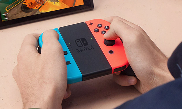 Närbild på två händer som håller i en Nintendo Switch-enhet i handhållet läge. Röd på ena sidan och blå på andra. 