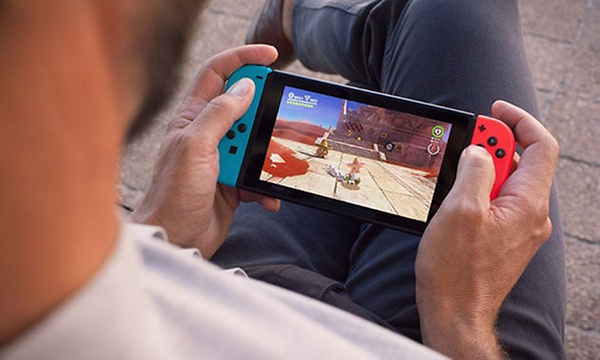 Bild ovanifrån bakom axeln på en man som sitter och spelar på en Nintendo Switch-enhet som han håller i händerna.